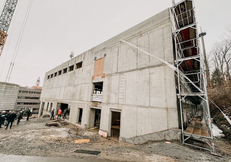 Ansicht Rohbau der Zweifachturnhalle für die Johann-Andreas-Schmeller-Mittelschule in Tirschenreuth. Personengruppe findet sich zum Richtfest am Gebäude ein.